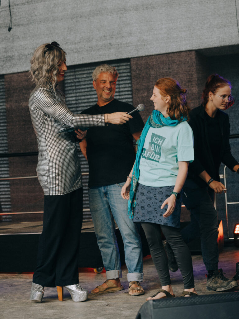 Moderator*in Janboris Ann-Kathrin Rätz interviewt ein Vorstandsmitglied von a+G und den Musikmaschine-Chef auf der Bühne.